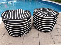 Two round black and white striped poufs beside pool