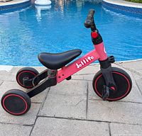 Side view of red and black Jollito tricycle by pool showing full frame, wheels, seat and pedals