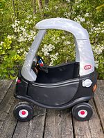 Side view of black and silver Cozy Coupe on wooden deck