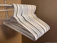 Stack of white heavy-duty plastic hangers on closet rod