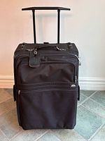 front view of black Samsonite wheeled suitcase showing telescoping handle and exterior pocket