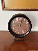 Front view of black metal round clock on stand showing full dial
