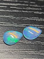 Top view of matching pear cabochon opals on dark background showing play of color