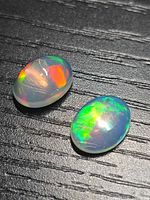 Both opals showing strong play-of-colour on textured black background