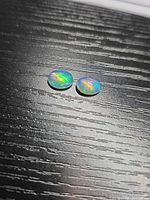 Pair of oval cabochon opals on dark surface showing play-of-colour