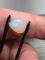 Pear-cut opal held in tweezers showing red and green fire