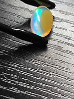 Oval Ethiopian crystal opal held by tweezers, showing blue flash and yellow phantom inclusion