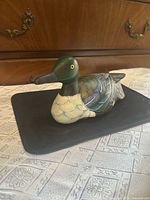 Front left view of carved wooden duck decoy showing green head, chest and body detail