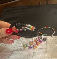 Lot overview showing black braided bracelet, multicolour bead bracelet and ten loose charm beads