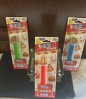 Front view of three sealed Pez Treats dispensers standing—pizza, burger, taco