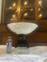 Front view of glass centerpiece on bronze stand with water bottle for scale