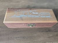 Closed wooden box with steam locomotive graphic and brass latch
