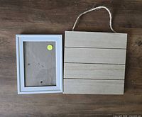 White photo frame and wooden plaque laying on wood surface
