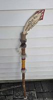 Full view of the wooden staff showing jawbone head, wrappings, feathers and painted details