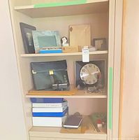 Overall shelf view showing clock, frames, boxes, binders, figurine