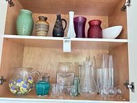 Cabinet shelves containing assorted glass and ceramic vases, pitchers and bowls in various colors and sizes