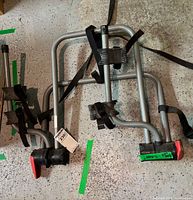 Full view of folded bike rack showing frame, straps, cradle arms, red end-caps