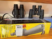 Two binoculars on shelf with Bushnell spotting scope box