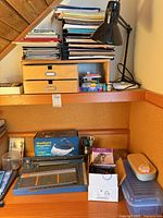 Overall desk with stacked paper, wooden drawers, desk lamp, Dahle trimmer, magnifier box