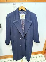Front view of navy overcoat hanging on hanger showing double-breasted buttons, lapel, and pockets