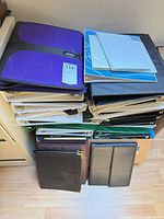 Stack of purple, black, green, white binders and zippered folders