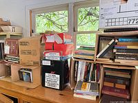 Multiple boxes and shelves of assorted books under window