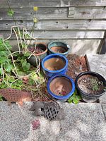 Group of ceramic planters in various colors and two metal ornaments on ground