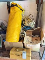 Yellow vinyl gear bag containing yellow twisted rope beside additional rope coils and boxes
