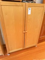 Front view of cabinet showing light maple veneer, two doors, round knobs, leg glides