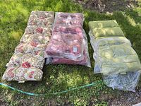 Three outdoor cushions laid on grass: floral bench, red lounge, green lounge
