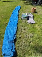 Blue car cover laid out with seat pad, green storage box and brown box