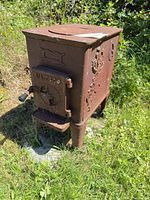 Full view of rusted cast iron stove outdoors showing overall form, top rings, legs, flue collar