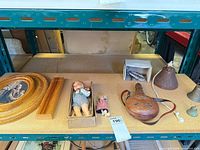 Shelf view showing frames, ruler, dolls, boxes, leather flask, metal items