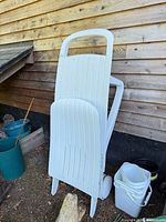 Full view of folded white plastic chaise lounge leaning against wall