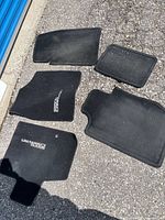 Five black Dodge Grand Caravan carpet floor mats laid out on pavement