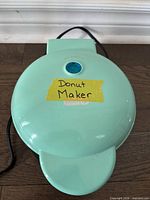Closed donut maker showing mint green exterior with blue indicator light and attached power cord