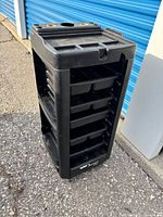 Full view of black plastic salon trolley on casters showing five trays and frame