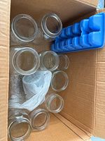 Cardboard box containing multiple clear glass mason jars and blue ice cube tray