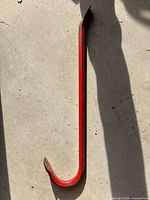 Full view of red crowbar lying on concrete floor, showing both hooked and chisel ends