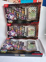 Two opened Paldean Fates collection boxes showing promo card and booster packs