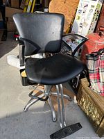 Front view of black vinyl salon chair showing seat, backrest, armrest, and footrest