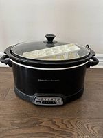 Front view of Hamilton Beach slow cooker with lid and ice cube tray resting on top