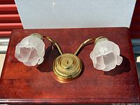 Full view of brass wall sconce with two frosted glass floral shades