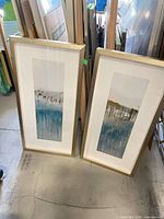 Two framed prints standing on floor