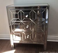 Front view of mirrored chest showing three drawers and geometric faceted mirror panels