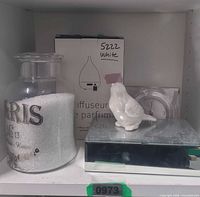 Shelf view of all five items together: bath salt jar, diffuser box, ceramic bird on mirrored box, acrylic clock