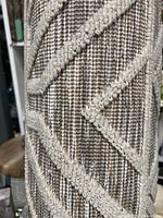 Close-up of rug surface showing beige raised geometric pattern on brown-beige woven background