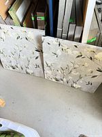 two square floral canvas prints leaning against shelving