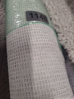 Rolled rug showing woven mesh backing with label