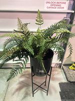 Full view of artificial fern plant in black pot on metal stand